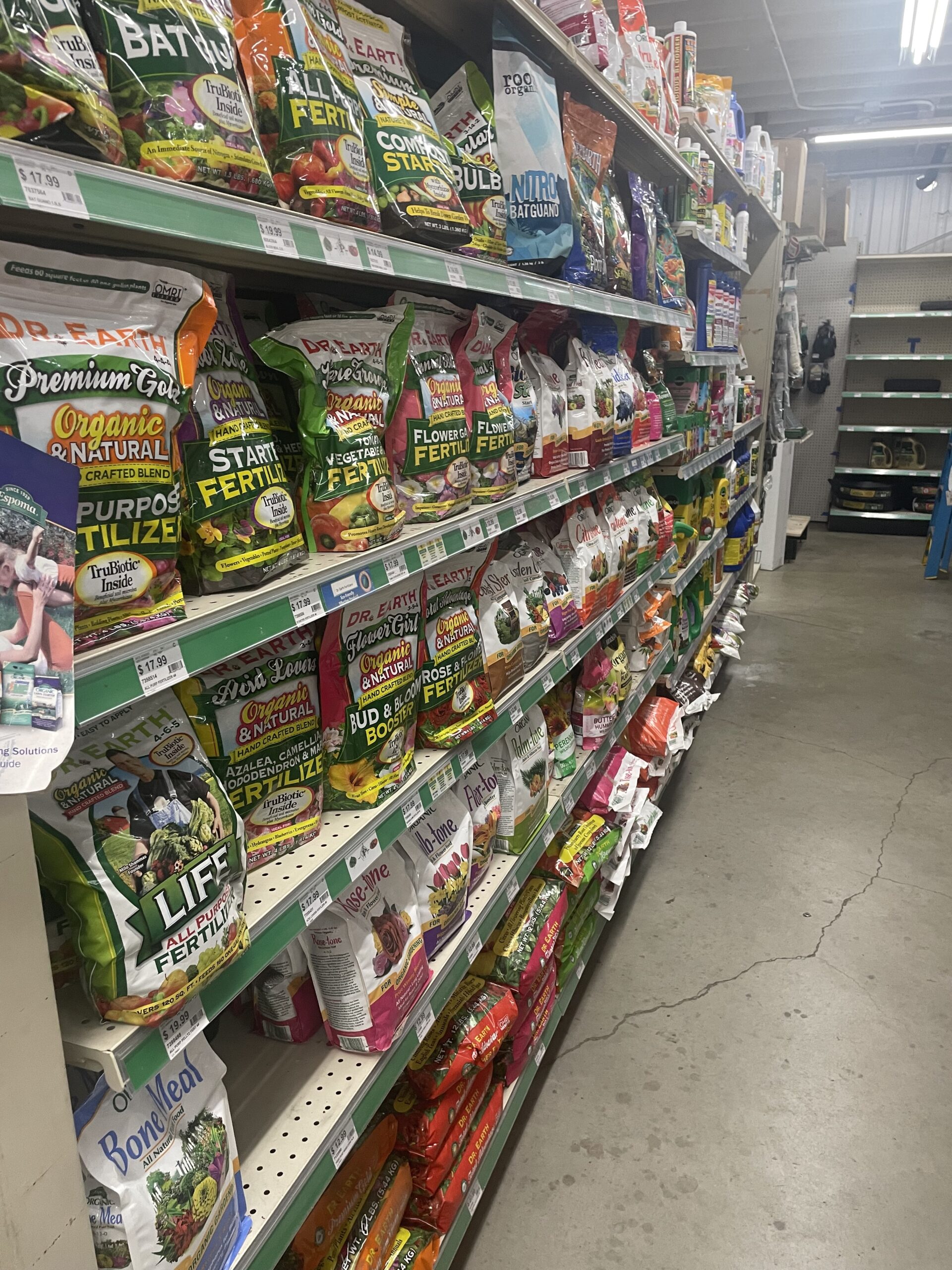 A garden center aisle displaying a wide selection of organic and synthetic fertilizers for vegetables, flowers, lawns, trees, and shrubs.
